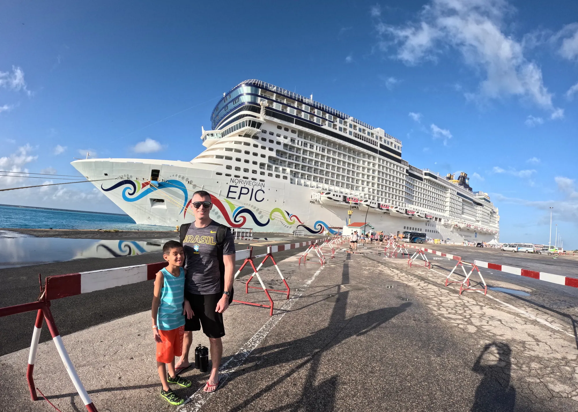 Mark and Ollie standing beside Norwegian Epic while the ship is docked in port.